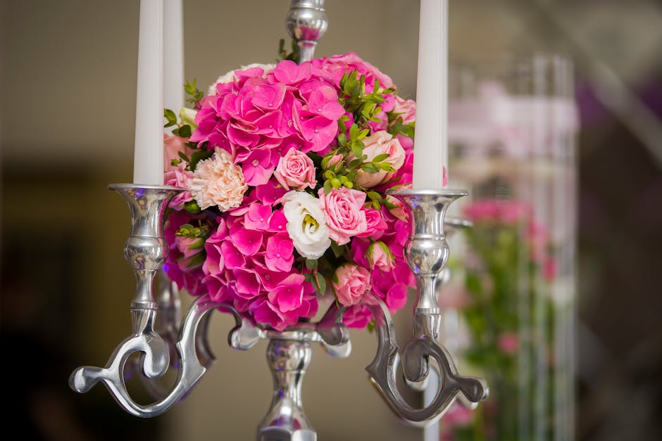 A floral arrangement featuring a lush bouquet of vibrant pink hydrangeas, soft pink roses, and delicate white lisianthus, expertly arranged with fresh green foliage. The bouquet is placed in a silver