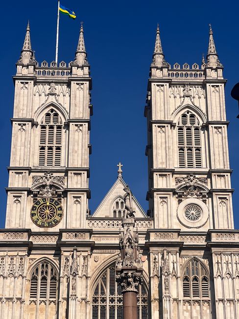 The image shows the front facade of Westminster Abbey with its distinctive Gothic architecture, including two tall spires, detailed stone carvings, arched windows, and a clock on the left tower. The s